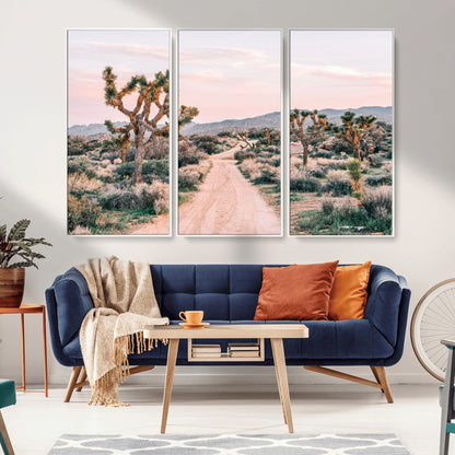 A dusty road winding through Joshua Tree National Park, framed by iconic twisted trees and warm desert tones under a soft pastel sky.