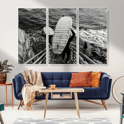Black and white photo of surfers carrying boards down a rugged cliffside stairway, capturing a bold and adventurous coastal scene.