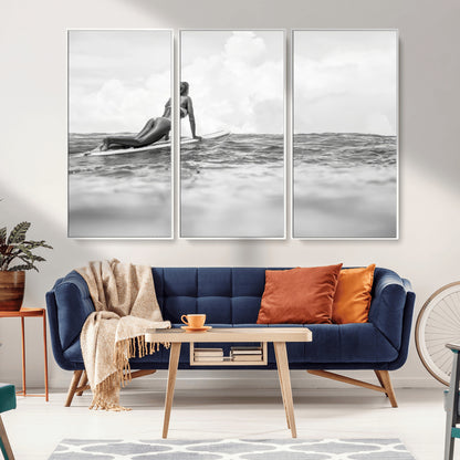A black and white ocean scene featuring a surfer girl waiting on her board, gazing at the horizon, capturing a tranquil and adventurous coastal moment.