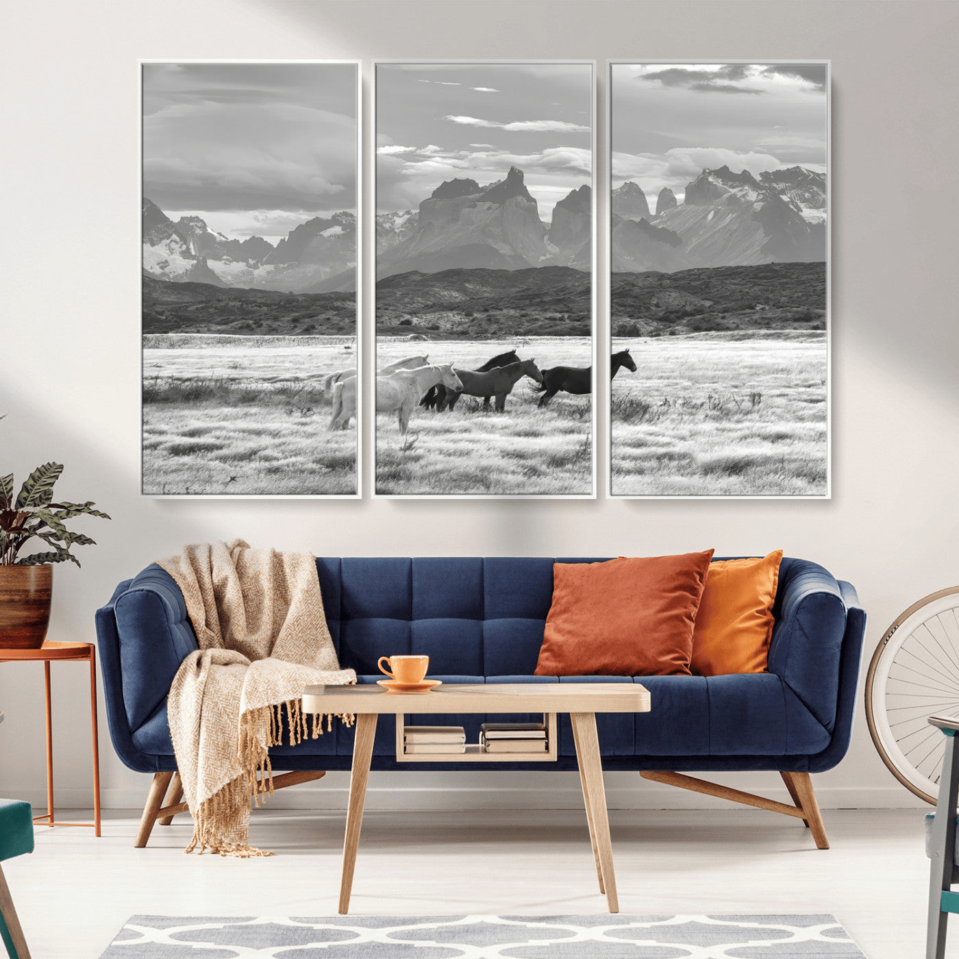 A black and white landscape of wild horses grazing in a vast grassland with towering mountains in the background, creating a moody and rustic western aesthetic.