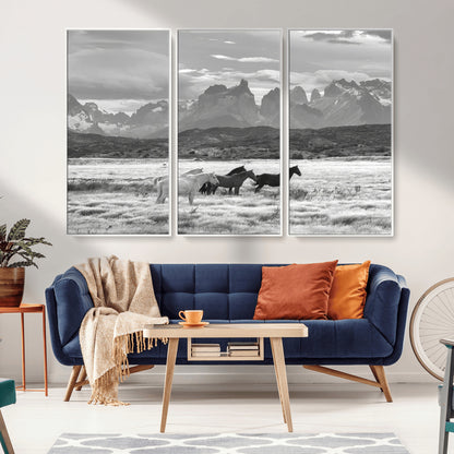 A black and white landscape of wild horses grazing in a vast grassland with towering mountains in the background, creating a moody and rustic western aesthetic.