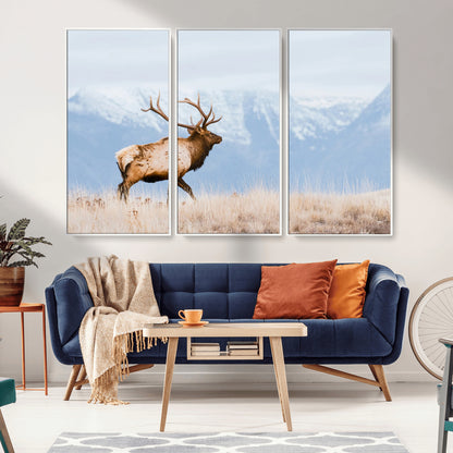 An elk walking on snowy grassland with majestic mountains in the background, ideal for rustic lodge or cabin wall decor.