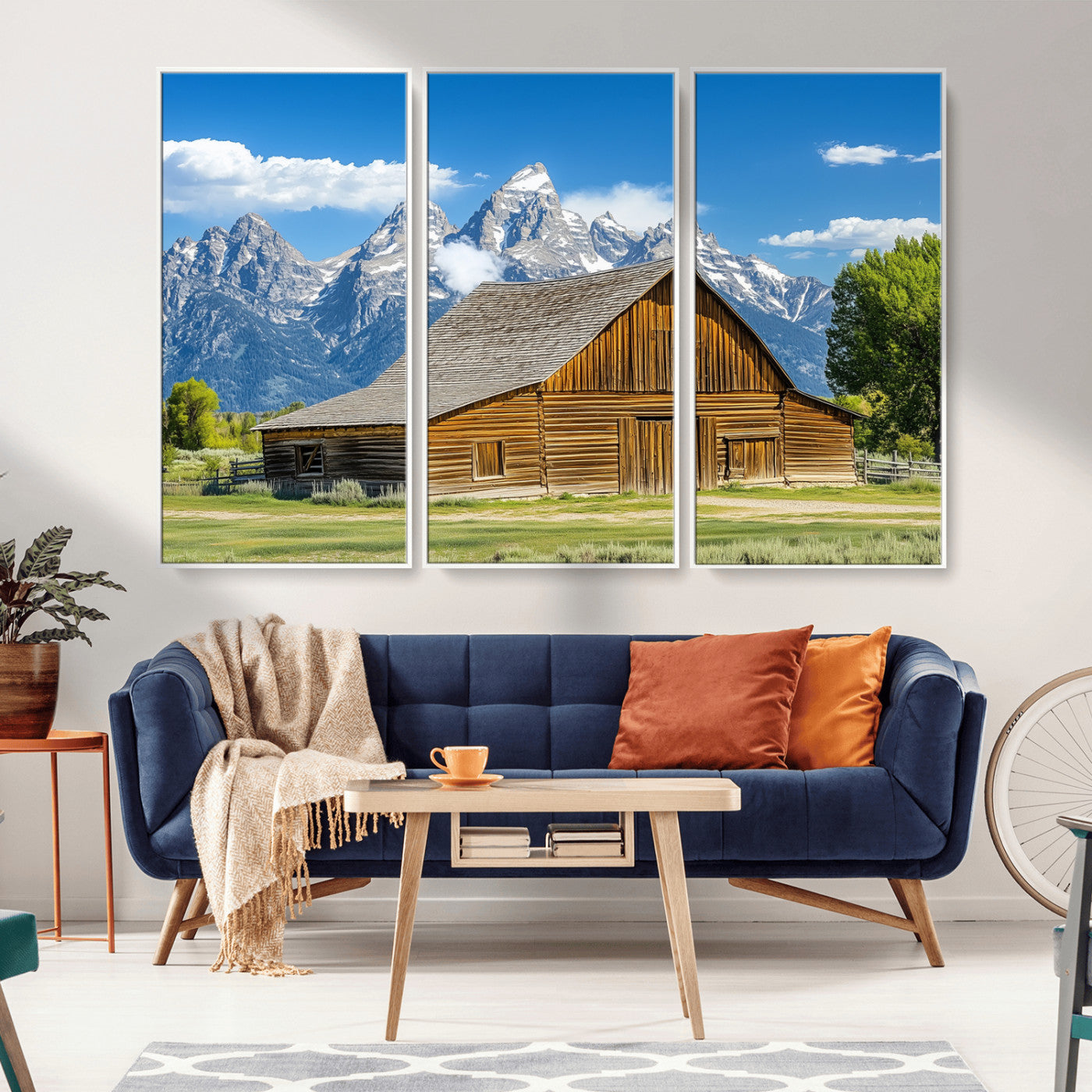 A rustic wooden barn sits in front of towering mountain peaks under a clear blue sky, perfect for farmhouse or cabin style interiors.