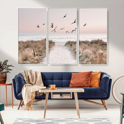 A peaceful coastal pathway leading to the ocean, with birds flying across a soft pastel sky, creating a calm and scenic beach atmosphere.