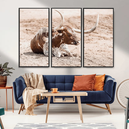 Texas Longhorn bull resting on dusty ground with warm tones, ideal for rustic western or farmhouse-themed wall decor.