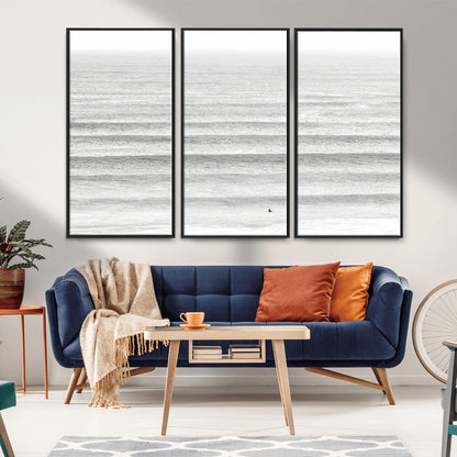 Monochrome photo of a lone surfer in calm layered waves, perfect for minimalist coastal or moody ocean-inspired wall decoration.