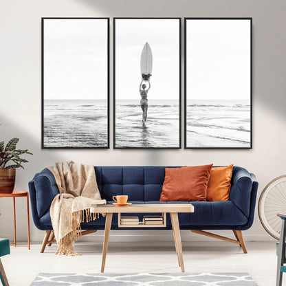Black and white image of a female surfer holding a surfboard above her head while walking toward the ocean, creating a minimalist and bold coastal aesthetic.