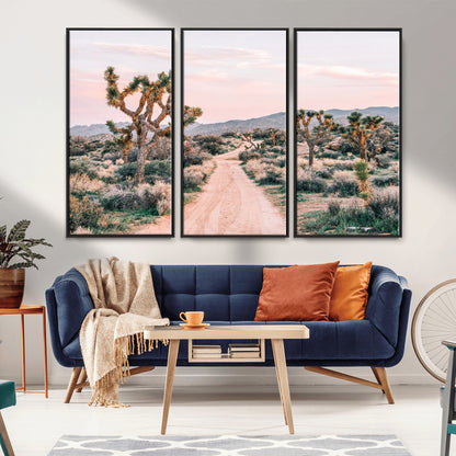 A dusty road winding through Joshua Tree National Park, framed by iconic twisted trees and warm desert tones under a soft pastel sky.