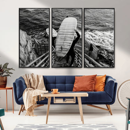 Black and white photo of surfers carrying boards down a rugged cliffside stairway, capturing a bold and adventurous coastal scene.