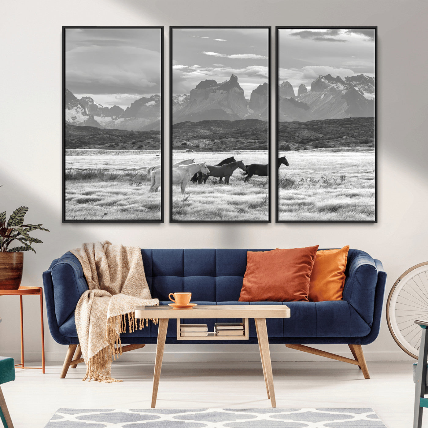 A black and white landscape of wild horses grazing in a vast grassland with towering mountains in the background, creating a moody and rustic western aesthetic.