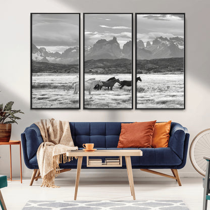 A black and white landscape of wild horses grazing in a vast grassland with towering mountains in the background, creating a moody and rustic western aesthetic.
