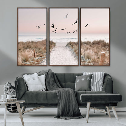 A peaceful coastal pathway leading to the ocean, with birds flying across a soft pastel sky, creating a calm and scenic beach atmosphere.