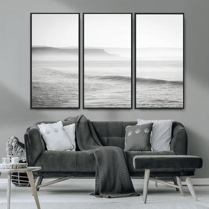 A black and white minimalist seascape featuring soft rolling waves and misty distant cliffs, creating a serene and timeless coastal atmosphere.