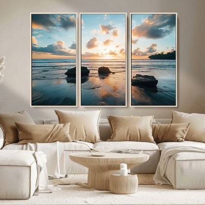 A serene beach at sunset with vibrant clouds, calm water, and rocks in the foreground reflecting the warm colors of the setting sun.