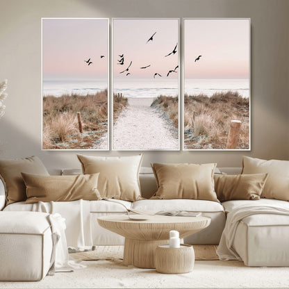 A peaceful coastal pathway leading to the ocean, with birds flying across a soft pastel sky, creating a calm and scenic beach atmosphere.