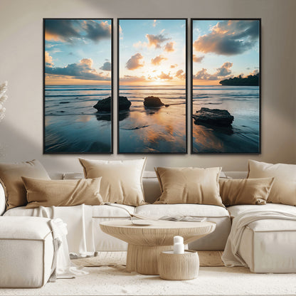 A serene beach at sunset with vibrant clouds, calm water, and rocks in the foreground reflecting the warm colors of the setting sun.