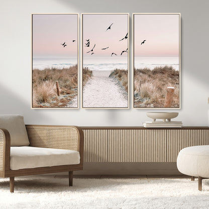 A peaceful coastal pathway leading to the ocean, with birds flying across a soft pastel sky, creating a calm and scenic beach atmosphere.