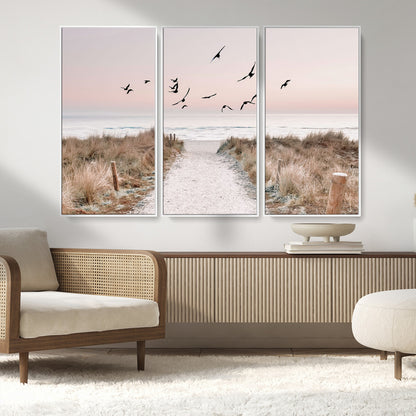 A peaceful coastal pathway leading to the ocean, with birds flying across a soft pastel sky, creating a calm and scenic beach atmosphere.