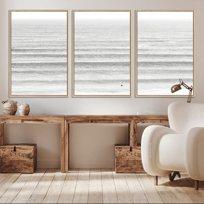 Monochrome photo of a lone surfer in calm layered waves, perfect for minimalist coastal or moody ocean-inspired wall decoration.