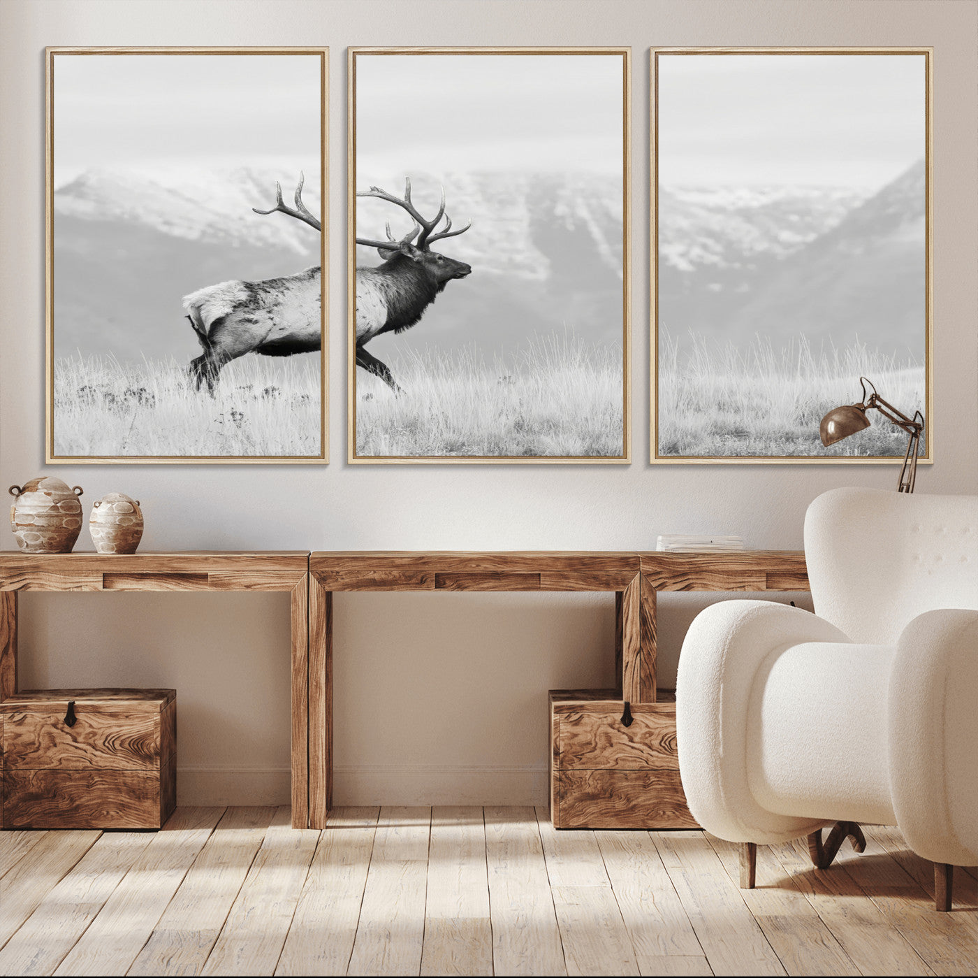 Black and white photograph of a majestic elk standing in a grassy field with snow-capped mountains in the background, creating a bold and rustic wilderness scene.