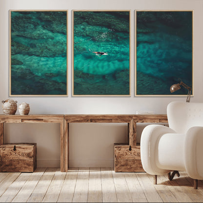 An aerial view of a solo surfer paddling through crystal-clear turquoise waters over a sunlit reef, capturing the beauty and serenity of open water surfing.