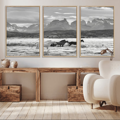 A black and white landscape of wild horses grazing in a vast grassland with towering mountains in the background, creating a moody and rustic western aesthetic.