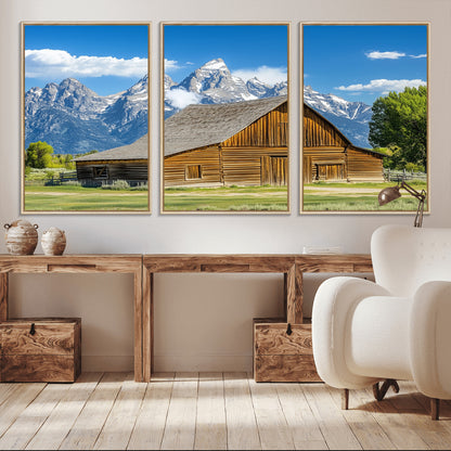 A rustic wooden barn sits in front of towering mountain peaks under a clear blue sky, perfect for farmhouse or cabin style interiors.