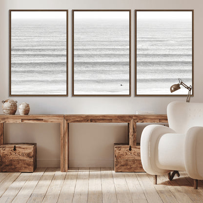 Monochrome photo of a lone surfer in calm layered waves, perfect for minimalist coastal or moody ocean-inspired wall decoration.