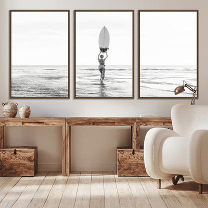 Black and white image of a female surfer holding a surfboard above her head while walking toward the ocean, creating a minimalist and bold coastal aesthetic.