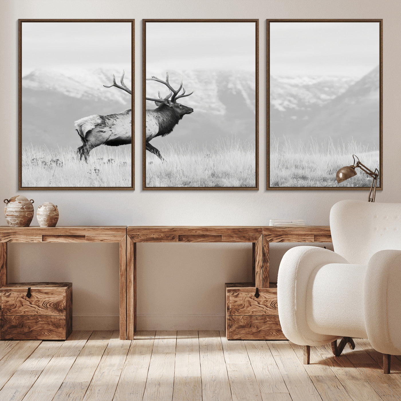 Black and white photograph of a majestic elk standing in a grassy field with snow-capped mountains in the background, creating a bold and rustic wilderness scene.