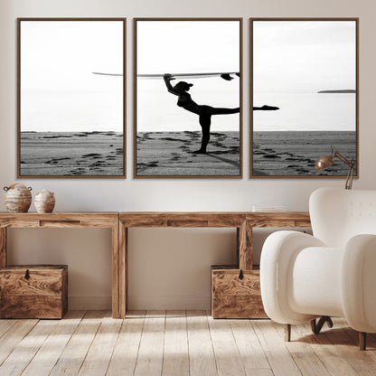 A woman balances a surfboard on her head while striking a yoga pose on the beach, silhouetted against a calm ocean horizon.