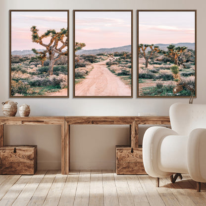 A dusty road winding through Joshua Tree National Park, framed by iconic twisted trees and warm desert tones under a soft pastel sky.