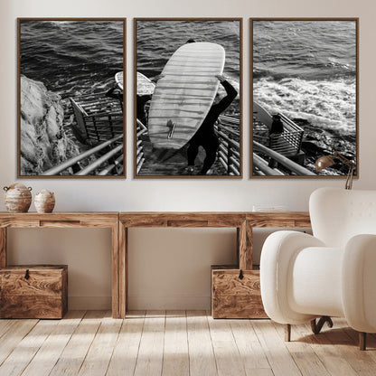 Black and white photo of surfers carrying boards down a rugged cliffside stairway, capturing a bold and adventurous coastal scene.