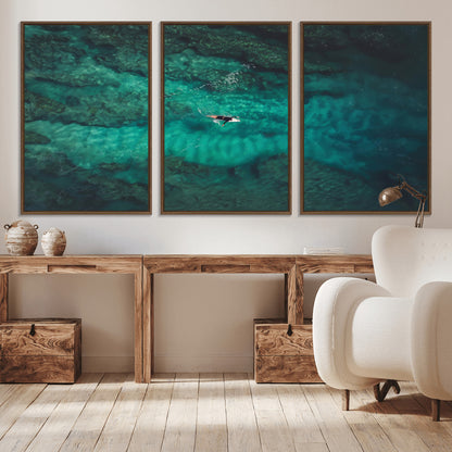 An aerial view of a solo surfer paddling through crystal-clear turquoise waters over a sunlit reef, capturing the beauty and serenity of open water surfing.