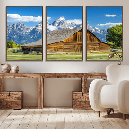 A rustic wooden barn sits in front of towering mountain peaks under a clear blue sky, perfect for farmhouse or cabin style interiors.