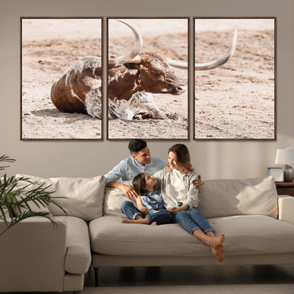 Texas Longhorn bull resting on dusty ground with warm tones, ideal for rustic western or farmhouse-themed wall decor.
