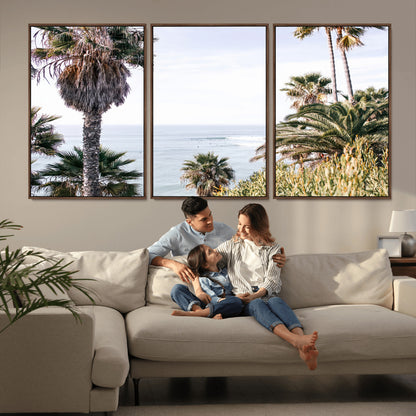 Scenic coastal view with tall palm trees overlooking a calm ocean, soft blue waves, and surfers in the distance, creating a peaceful tropical vibe.