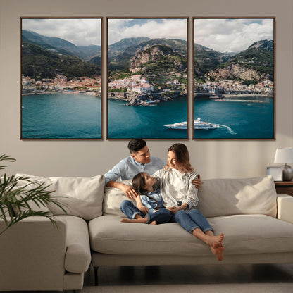 Aerial view of Amalfi Coast, Italy, with colorful hillside houses, lush green mountains, and a luxury yacht sailing in turquoise waters.