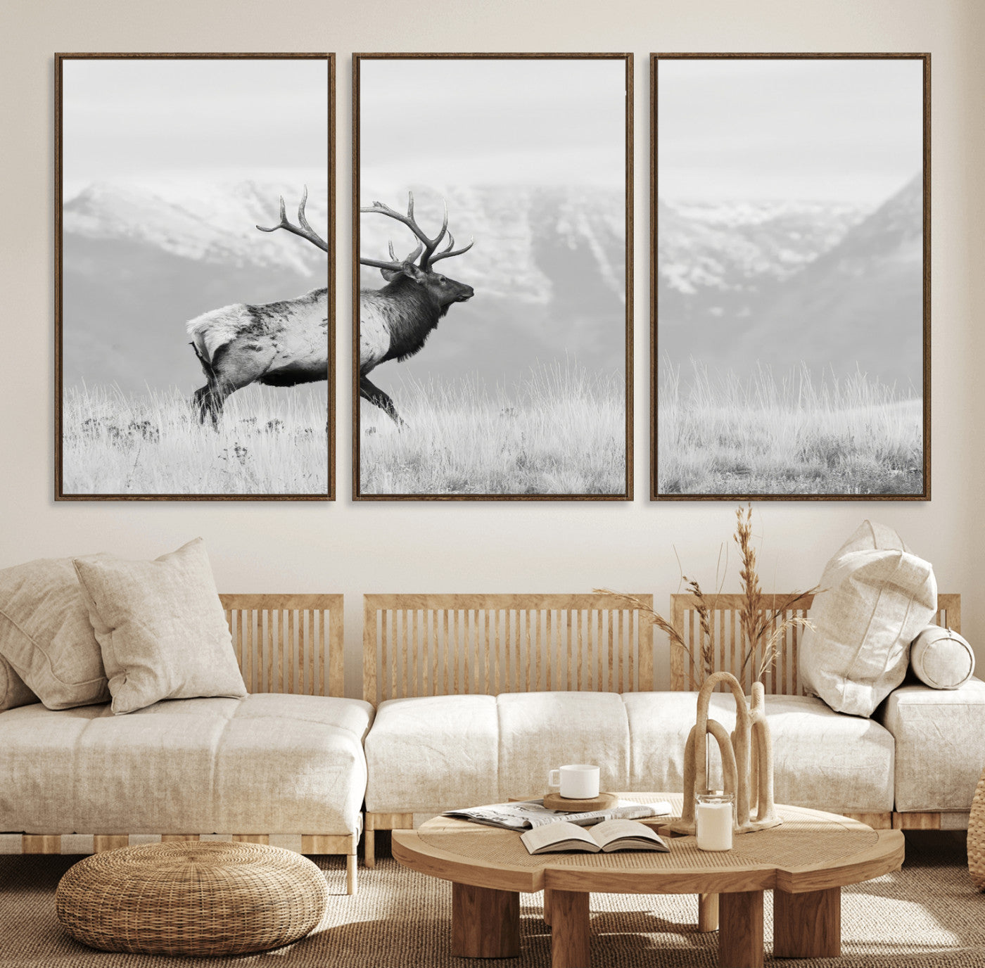 Black and white photograph of a majestic elk standing in a grassy field with snow-capped mountains in the background, creating a bold and rustic wilderness scene.
