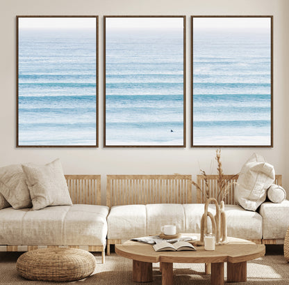 Minimalist ocean view with soft blue waves and a lone surfer, creating a serene and airy coastal aesthetic, perfect for tranquil home decor.