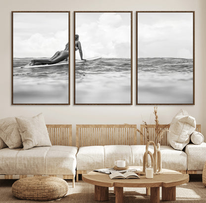 A black and white ocean scene featuring a surfer girl waiting on her board, gazing at the horizon, capturing a tranquil and adventurous coastal moment.