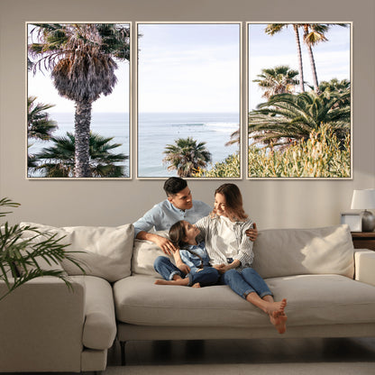 Scenic coastal view with tall palm trees overlooking a calm ocean, soft blue waves, and surfers in the distance, creating a peaceful tropical vibe.
