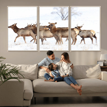 A group of elk standing on snowy terrain with a tree in the background, perfect for rustic or lodge-style winter wall decor.
