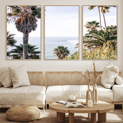Scenic coastal view with tall palm trees overlooking a calm ocean, soft blue waves, and surfers in the distance, creating a peaceful tropical vibe.