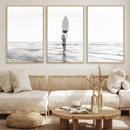 Black and white image of a female surfer holding a surfboard above her head while walking toward the ocean, creating a minimalist and bold coastal aesthetic.