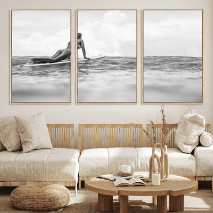 A black and white ocean scene featuring a surfer girl waiting on her board, gazing at the horizon, capturing a tranquil and adventurous coastal moment.
