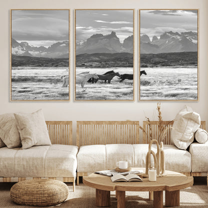 A black and white landscape of wild horses grazing in a vast grassland with towering mountains in the background, creating a moody and rustic western aesthetic.
