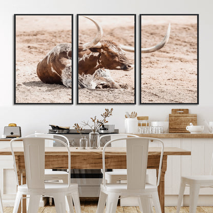 Texas Longhorn bull resting on dusty ground with warm tones, ideal for rustic western or farmhouse-themed wall decor.