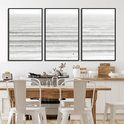 Monochrome photo of a lone surfer in calm layered waves, perfect for minimalist coastal or moody ocean-inspired wall decoration.