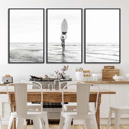 Black and white image of a female surfer holding a surfboard above her head while walking toward the ocean, creating a minimalist and bold coastal aesthetic.
